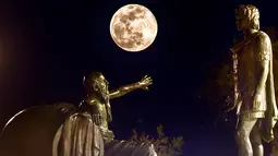 Fenomena super snow moon terlihat di antara patung Alexander Agung (kanan) dan Diogenes of Sinope (kiri) di Corinth, Yunani, Selasa (19/2). Super snow moon menampakkan diri di berbagai belahan dunia. (Valerie GACHE/AFP)