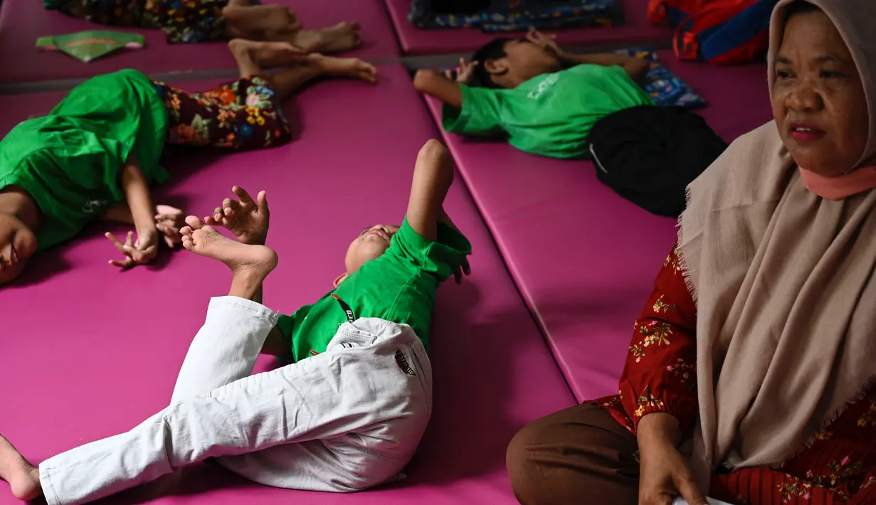 Seorang anak penderita cerebral palsy berbaring di samping ibunya saat berkumpul bersama keluarga untuk memperingati Hari Cerebral Palsy Sedunia di pusat fisioterapi Yayasan Sahabat Difabel di Banda Aceh (6/10/2021). (AFP/Chaideer Mahyuddin)