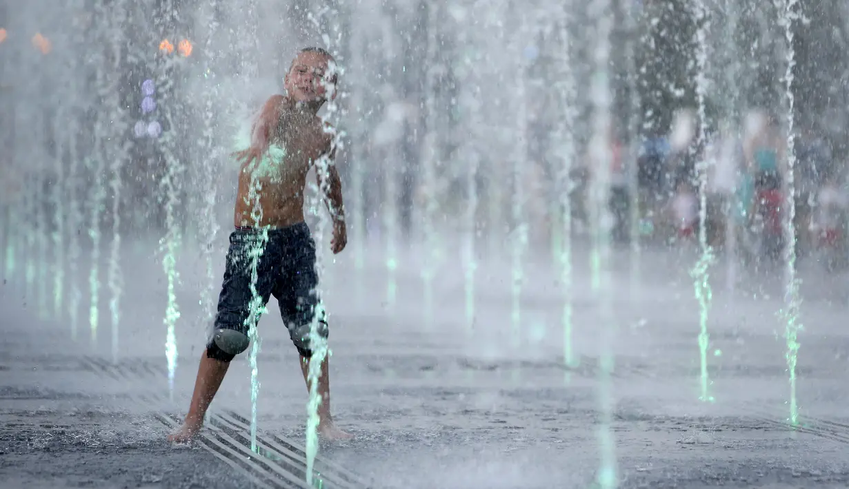 Seorang anak lelaki bermain diantara air mancur saat menikmati musim panas di taman Gorky, Moskow, Rusia, Minggu (9/8/2015). (REUTERS/Sergei Karpukhin)