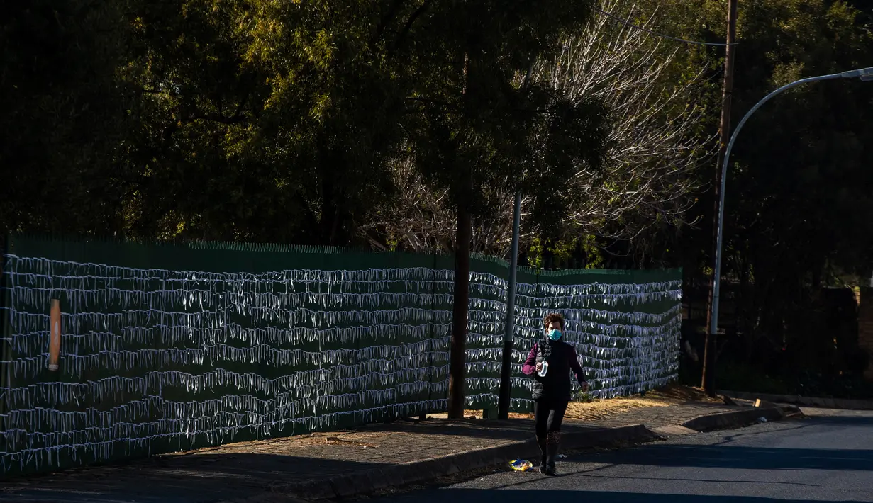 Pejalan kaki melewati pita-pita yang telah diikatkan ke pagar gereja St James Presbyterian di Bedford Gardens, Johannesburg, Rabu (29/7/2020). Pita tersebut mewakili warga Afrika Selatan yang meninggal akibat virus corona COVID-19. (AP Photo/Themba Hadebe)