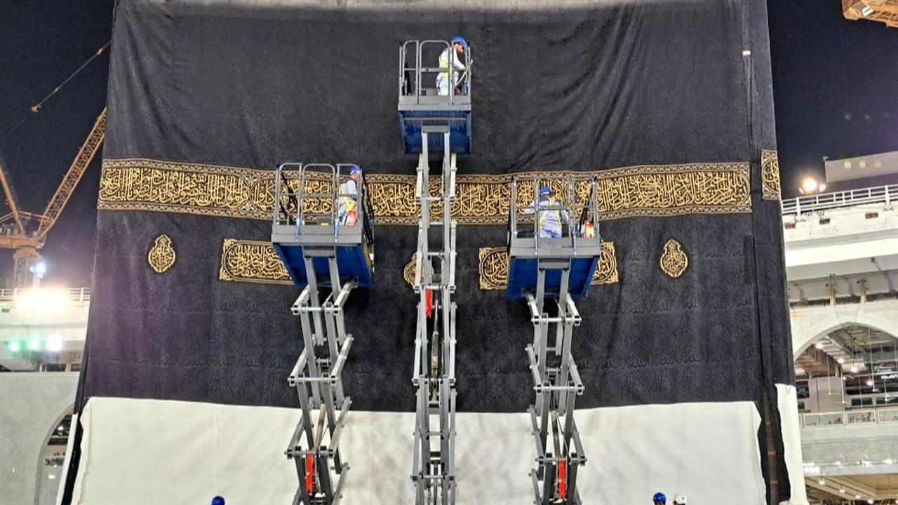 Puluhan petugas berjubah putih berada di atap Ka'bah menarik kain Kiswah yang baru satu persatu tiap sisi.
