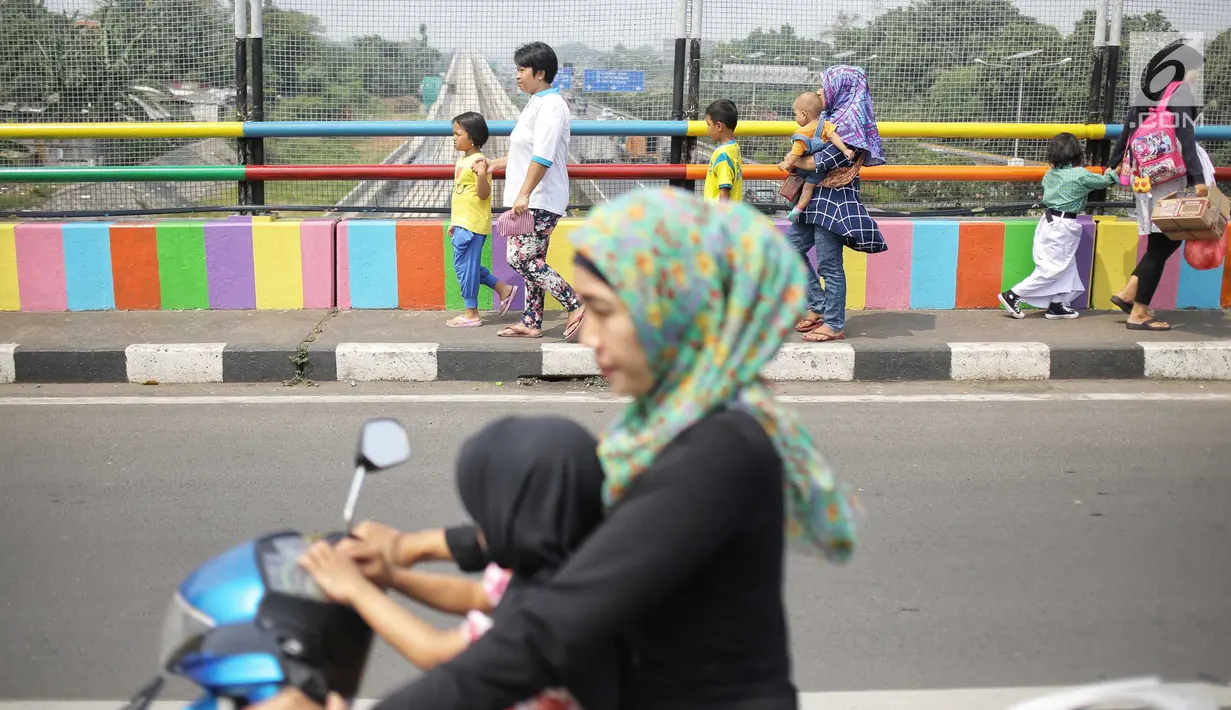 Pejalan kaki melintasi jembatan layang yang dicat dengan warna-warna ceria di Kampung Makasar, Jakarta, Kamis (26/7).  Pengecatan dilakukan guna mempercantik dan menyambut Asian Games 2018 pada Agustus mendatang.  (Liputan6.com/Faizal Fanani)