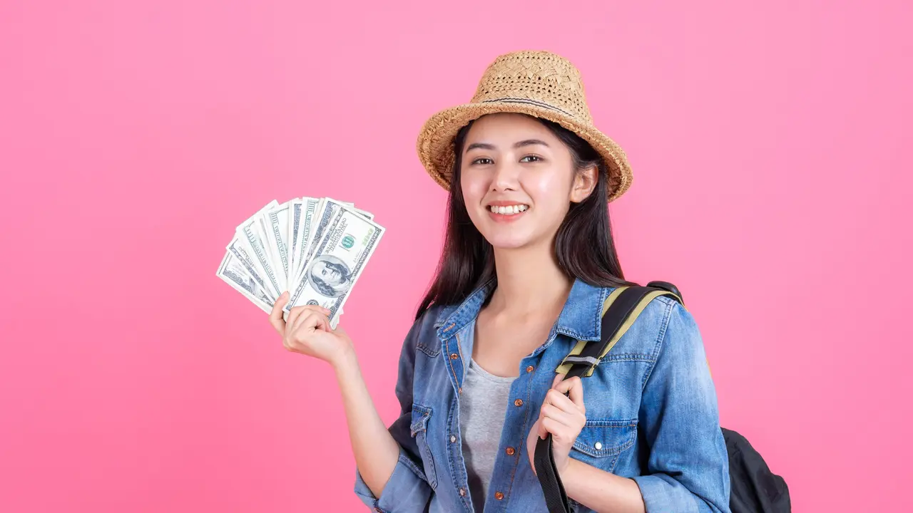 Seorang perempuan dengan pakaian berlibur sedang memegang sejumlah uang (Foto Dok: Freepik/jcomp)