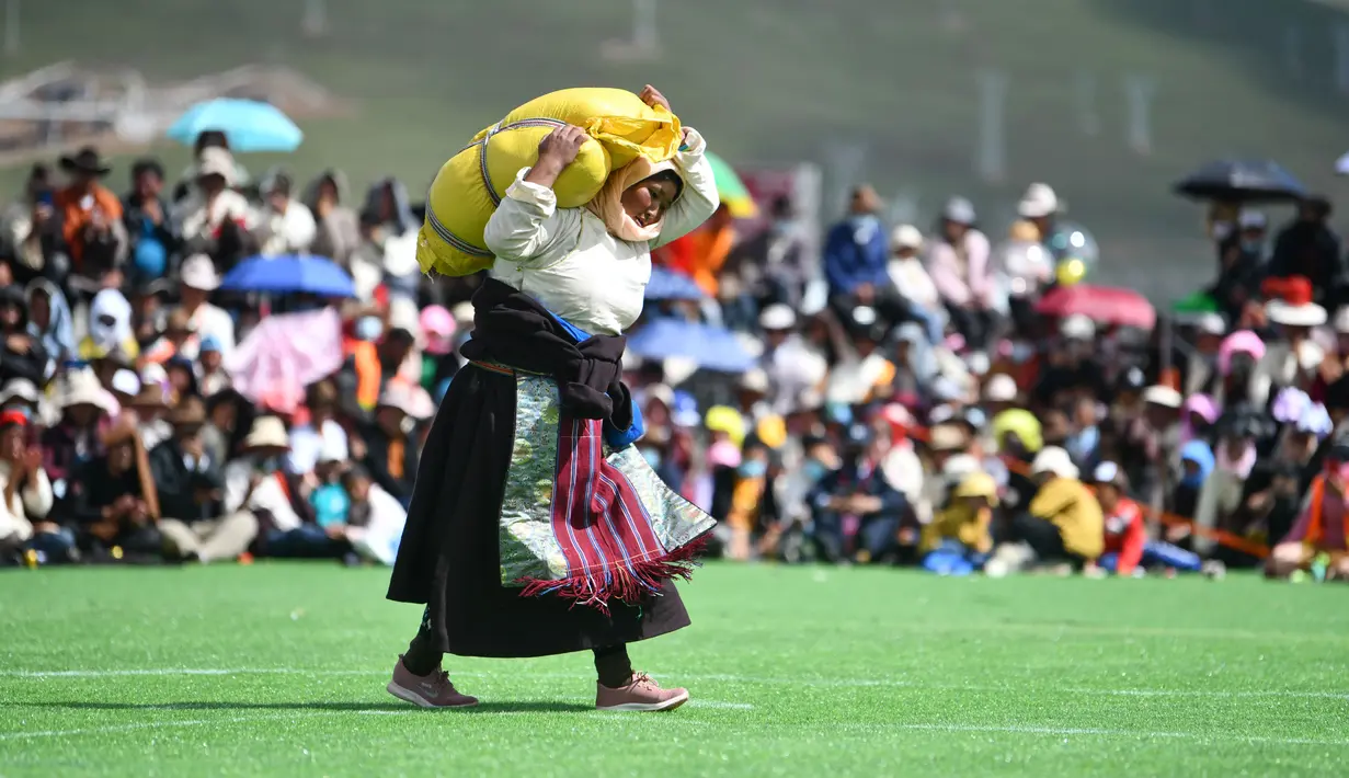 Seorang partisipan mengangkat karung berisi barli dataran tinggi dalam sebuah kompetisi yang digelar saat festival balap kuda Dangjiren di Wilayah Damxung, Daerah Otonom Tibet, China barat daya, pada 11 Agustus 2020. (Xinhua/Jigme Dorje)