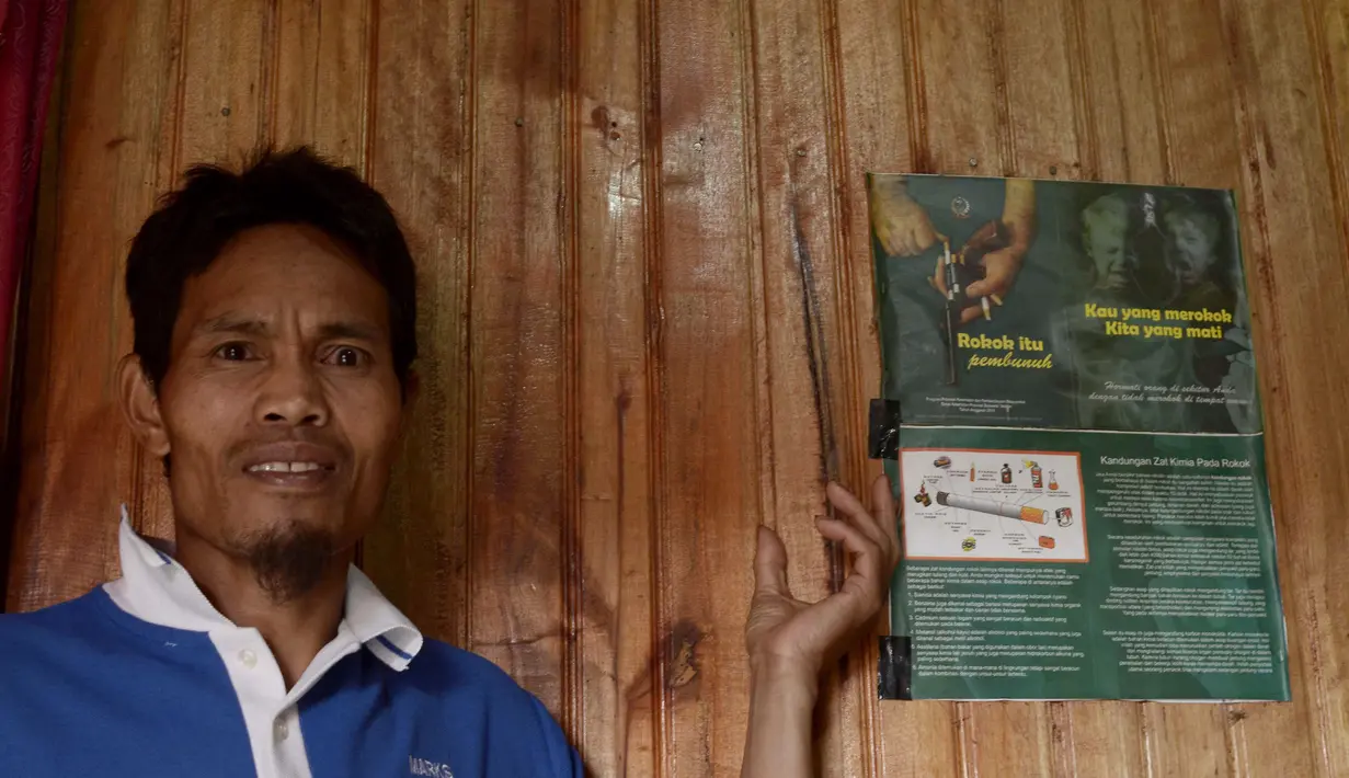 Kepala desa, Abdul Wahid berdiri di samping poster kampanye anti merokok yang berbunyi "Rokok itu pembunuh", "Kau yang merokok, kita yang mati" di rumahnya di Desa Bone-Bone, Enrekang, Sulawesi Selatan, 20 Desember 2015. (Cening Unru/AFP)