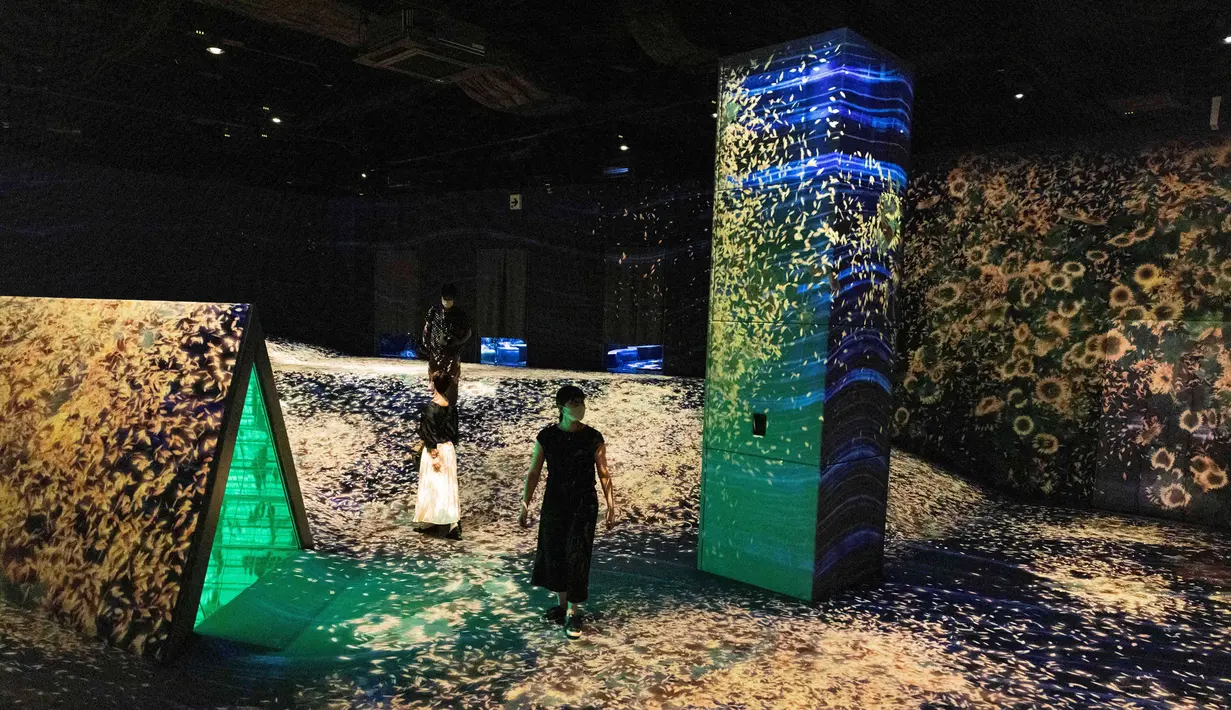 Seorang anggota staf dan anggota pers berdiri di instalasi digital interaktif bernama "Shifting Valley, Living Creatures of Flowers, Symbiotic Lives" selama pratinjau media "teamLab Forest" di gedung hiburan BOSS E・ZO FUKUOKA di Fukuoka, Jepang, Jumat (16/7/2021). (YUKI IWAMURA/AFP)