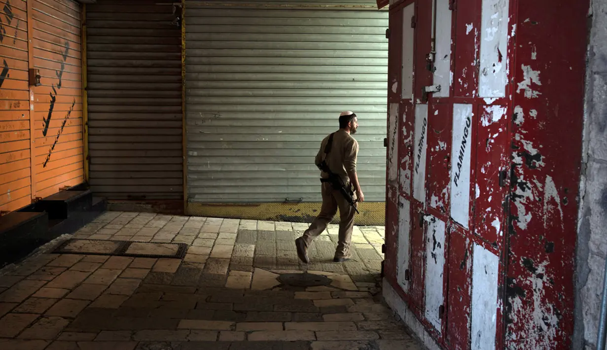 Seorang pria Yahudi bersenjata berjalan melalui deretan etalase toko yang ditutup untuk pemogokan umum yang menyerukan gencatan senjata di Gaza di Kota Tua Yerusalem, Senin (11/12/2023). (AP Photo/Maya Alleruzzo)