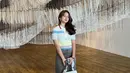 Inspirasi outfit untuk museum date dari Rebecca Klopper. Ia mengenakan atasan lengan pendek bergaris bernuansa biru, dipadu dengan rok cokelat, sandal slip on, dan tas. Foto: Instagram.