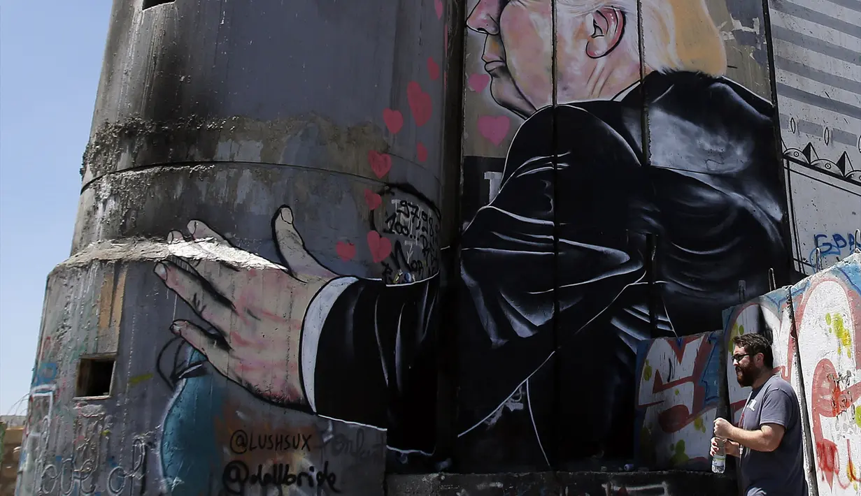 Seorang pria berjalan melewati grafiti yang menggambarkan Presiden AS Donald Trump di tembok pemisah Israel - Palestina di kota Bethlehem (4/8). (AFP Photo/Musa Al Shaer)