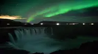 Langit berhias aurora borealis atau Cahaya Utara terlihat di atas air terjun Godafoss di Thingeyjarsveit, Islandia, 14 Oktober 2018. Lukisan abstrak alam semesta dari tabrakan spektrum warna Aurora Borealis begitu spektakuler. (Mariana SUAREZ/AFP)
