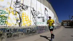 Peserta berlari menyusuri tembok pemisah Israel selama Right to Movement Maraton di kota Bethlehem, Palestina, Jumat (1/4). Tembok ini menjadi sarana bagi seniman jalanan untuk menuangkan keahliannya. (REUTERS / Ammar Awad)