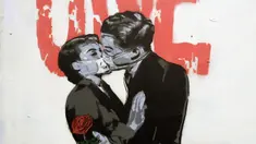 Mural karya Unify Artist menampilkan sepasang kekasih berciuman dengan mengenakan masker karena pandemi virus corona COVID-19 terlihat pada sebuah pagar di London, Inggris, Selasa (7/4/2020). (AP Photo/Matt Dunham)