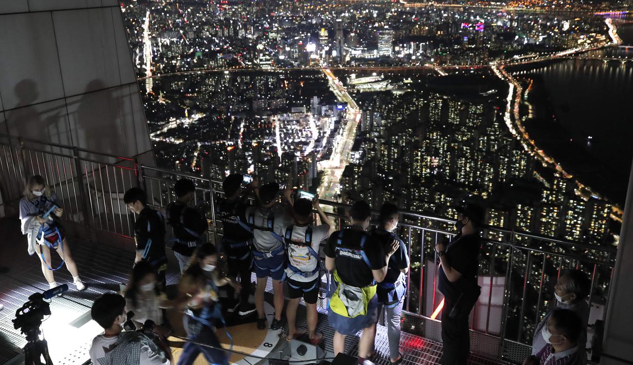 Orang-orang yang memakai masker wajah untuk membantu melindungi dari penyebaran virus korona, melihat pemandangan malam Seoul saat mereka menginap di tempat berkemah semalam di atap gedung pencakar langit di Seoul, Korea Selatan (7/8/2020).  (AP Photo/Lee Jin-man)