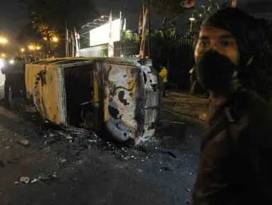 Seorang pemuda berdiri di depan mobil yang telah hangus terbakar saat terjadi bentrokan di kawasan Jalan Diponegoro, Salemba, Jakarta, Kamis (29/3) malam. Sejumlah pengunjuk rasa yang menolak kenaikan harga BBM diamankan, sementara beberapa mahasiswa dan personel kepolisian terluka dalam peristiwa bentrok tersebut. (Antara)