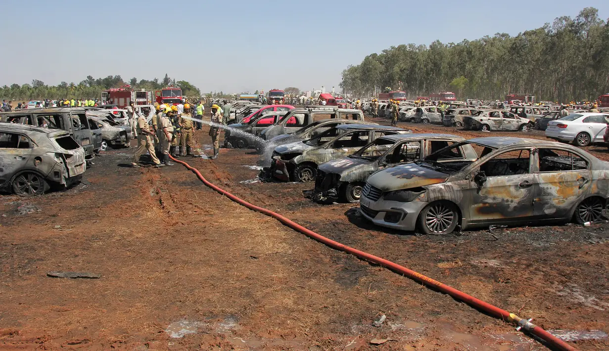 Petugas pemadam kebakaran memadamkan api yang membakar deretan mobil di area parkir pameran dirgantara Aero India 2019, Bangalore, India, Sabtu (23/2). Kebakaran diperparah dengan embusan angin yang kencang. (STR/AFP)