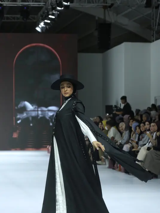 Ia terlihat elegan dalam pakaian monokrom, mengenakan dress panjang putih berkancing dengan aksen lengan puff. Dress tersebut dipadukan dengan outer panjang berkancing di bagian depan, yang memiliki desain cape pada lengan. Nabila juga mengenakan topi koboi hitam yang serasi dengan kerudung lilitnya.  [Dok/Fimela/Adrian Utama P].
