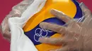 Petugas mengenakan sarung tangan plastik dan kain saat mendisinfeksi bola voli jelang pembukaan pertandingan voli Olimpiade Tokyo 2020 di Ariake Arena, Tokyo, Jepang, Jumat (23/7/2021). Olimpiade Tokyo 2020 digelar dengan penerapan protokol kesehatan ketat. (AP Photo/Frank Augstein)