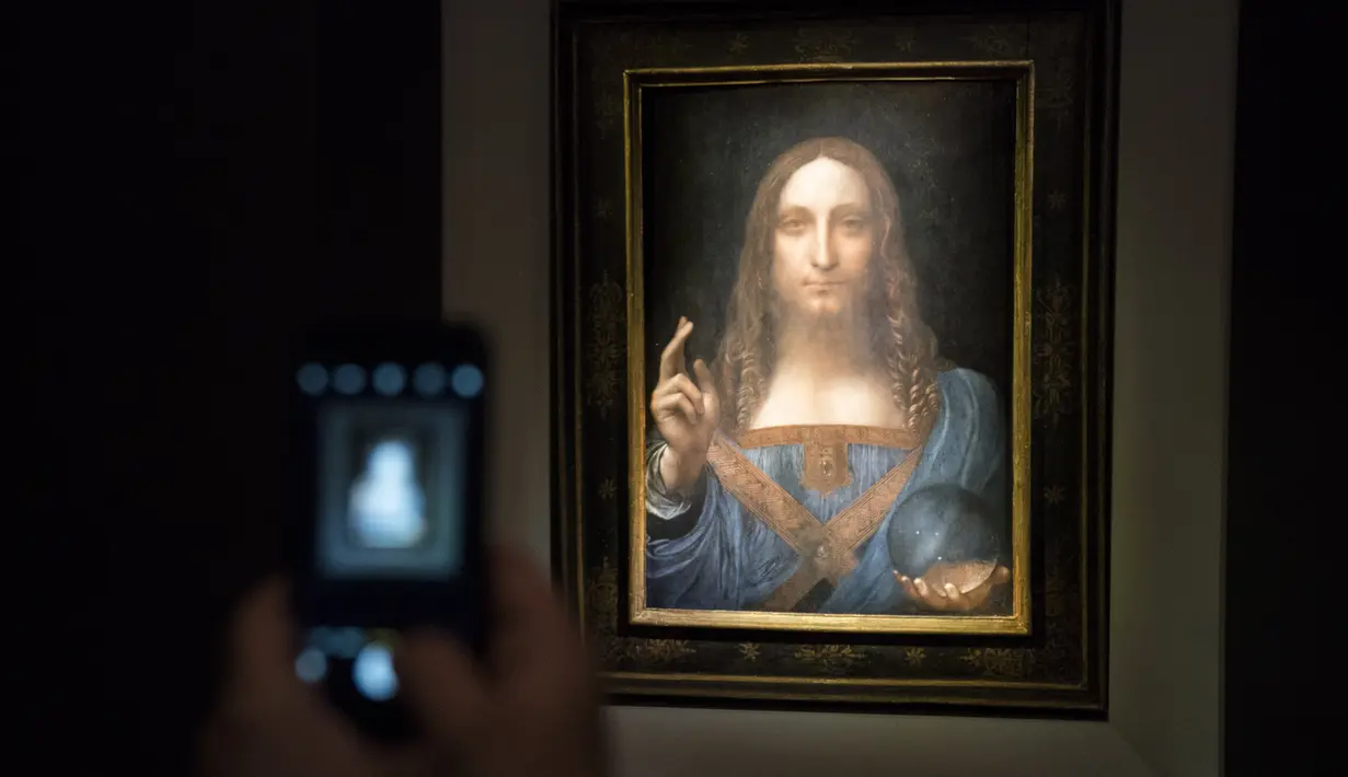 Seorang pengunjung mengambil foto lukisan 'Salvator Mundi' karya Leonardo da Vinci di Christie's New York Auction House, New York City (15/11). Lukisan wajah Yesus Kristus karya da Vinci ini terjual seharga US$ 450,3 juta. (Drew Angerer/Getty Images/AFP)