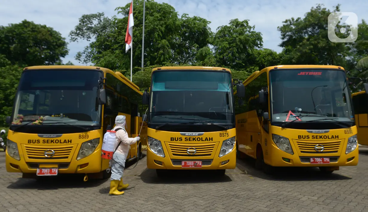 Petugas ber-APD menyemprotkan disinfektan pada bus sekolah di Posko Gabungan PSBB dan Gakplin Protkes, Puskesmas Jatinegara, Jakarta, (22/9/2020). Sejumlah unit bus sekolah kini dialihfungsikan menjadi kendaraan untuk mengantar pasien Covid-19 berstatus menuju Wisma Atlet. (merdeka.com/Imam Buhori)