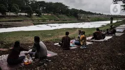 Warga bersantai di dekat limbah busa yang memenuhi aliran Kanal Banjir Timur (KBT), Duren Sawit, Jakarta, Kamis (2/7/2020). Busa yang memenuhi aliran KBT akibat limbah pabrik dan rumah tangga sejak dua minggu lalu itu menjadi tontonan warga meski menimbulkan bau tak sedap (merdeka.com/Iqbal Nugroho)