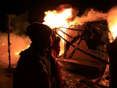 Sejumlah imigran berdiri melihat tempat tinggalnya yang dibakar pihak berwenang Prancis saat pembongkaran kamp pengungsian di lahan kumuh yang dijuluki "Jungle" di Calais, Prancis (1/3). (REUTERS/Pascal Rossignol)