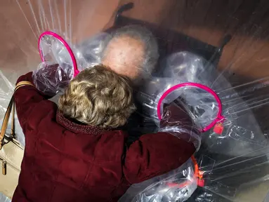 Diane Rossi (Kiri) memeluk suaminya, Arthur Rossi, melalui tenda pelukan di komunitas Crossroads Senior Living di Lakewood, Colorado, Jumat (26/2/2021). Tenda dengan penghalang plastik memungkinkan anggota keluarga terhubung secara fisik satu sama lain. (Michael Ciaglo/Getty Images/AFP)