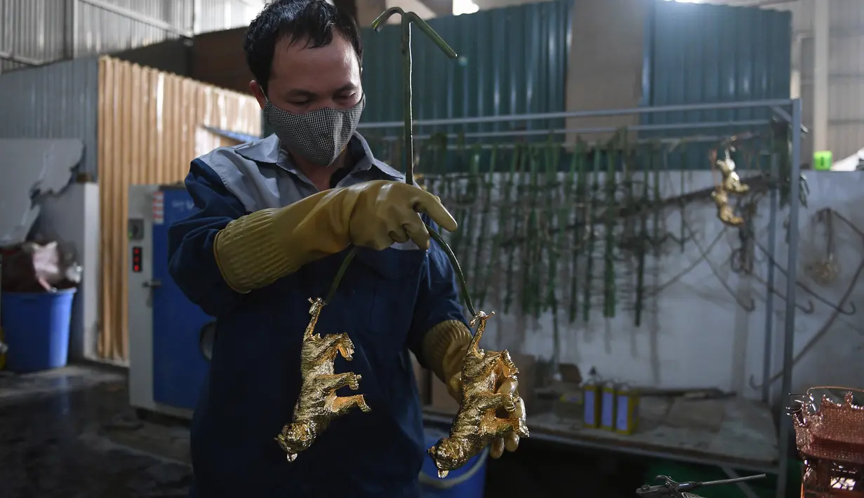 Seorang pekerja membawa model harimau berlapis emas menjelang Tahun Baru Imlek, yang ditandai sebagai Tahun Macan Air di sebuah bengkel di Hanoi, 19 Januari 2022. Di Vietnam, perayaan Tahun Baru China disebut Tet yang merupakan salah satu perayaan paling penting masyarakat di sana. (Nhac NGUYEN/AFP)