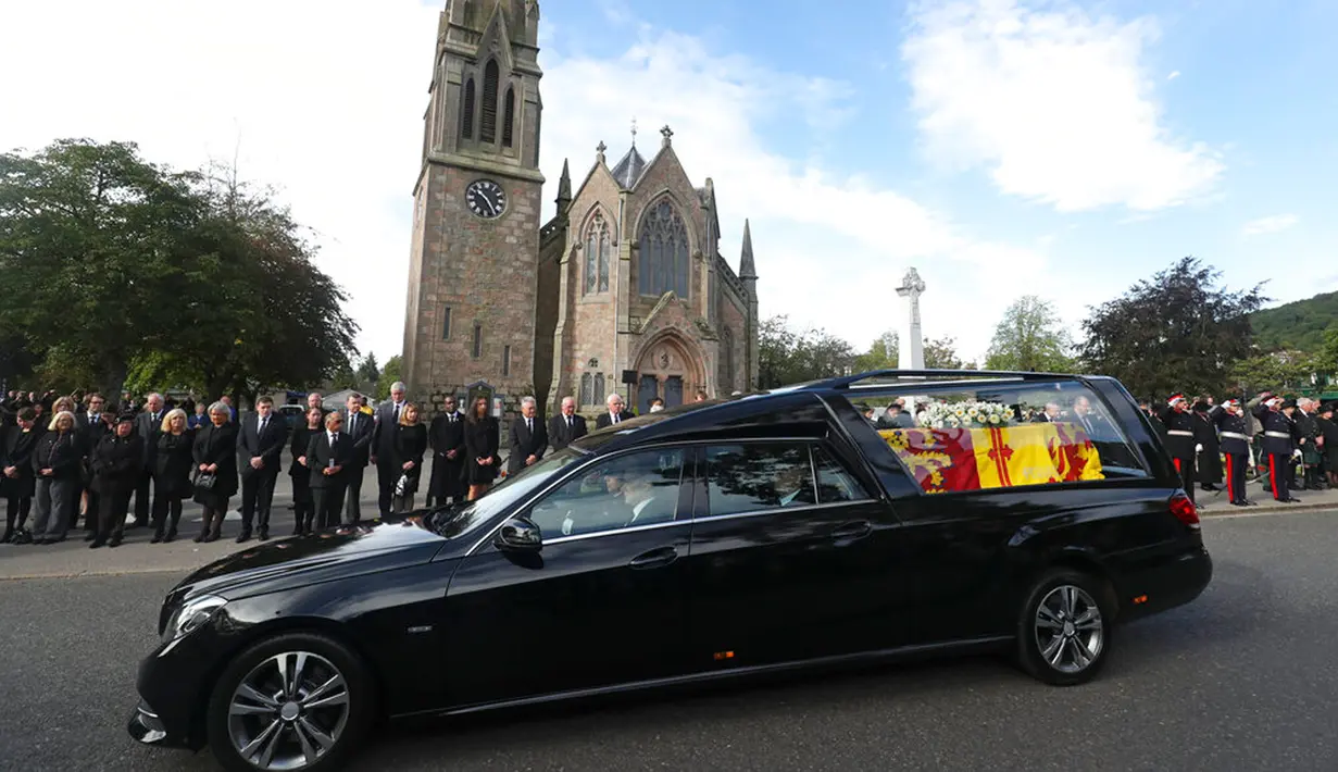 Warga berbaris saat mobil yang membawa peti berisi jenazah Ratu Elizabeth II melintas di Ballater, Skotlandia, Minggu (11/9/2022). Jenazah Ratu Elizabeth II diberangkatkan dari Kastil Balmoral ke Istana Holyroodhouse di Edinburgh sebelum nantinya akan dipindahkan ke London. (AP Photo/Scott Heppell)
