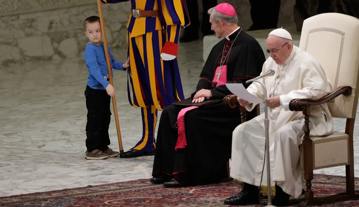 Seorang bocah menyentuh anggota penjaga Swiss saat Paus Fransiskus menyampaikan audensi mingguan di Vatikan, Rabu (28/11). Paus Fransiskus sedang berbicara di depan audiensi ketika bocah 6 tahun tersebut naik ke atas panggung. (AP/Gregorio Borgia)