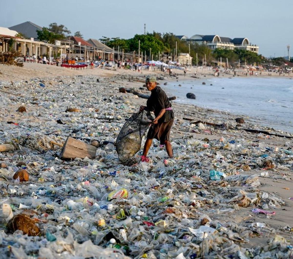 Seorang warga mengumpulkan sampah di Pantai Kedonganan, Kuta, Badung, Bali, Selasa (19/3/2024). Sampah kiriman yang terbawa ombak di lautan itu tampak menutupi hamparan pasir putih di Pantai Kedonganan.&nbsp;Sonny Tumbelaka/AFP