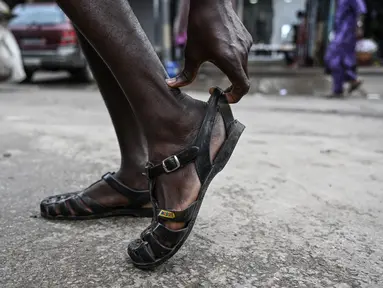 Seorang pria memakai sepatu Leke di Treichville, Abidjan, Pantai Gading pada 14 September 2023. Di Abidjan, musim hujan akan segera berakhir, tetapi orang-orang tidak pernah menyimpan "leke" mereka - sandal plastik yang murah dan kedap air, yang telah menjadi simbol identitas budaya Pantai Gading. (Sia KAMBOU / AFP)