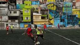 Aksi anak-anak saat bermain sepak bola di sebuah lapangan di Jardim Peri, Sao Paulo, Brasil, Minggu (20/5). Sebuah mural raksasa bergambar pemain sepak bola profesional Gabriel Jesus menghiasi permukiman mereka. (AP Photo/Andre Penner)