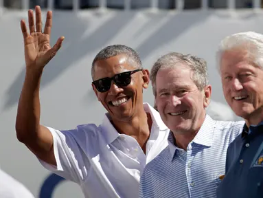 Mantan Presiden AS, Barack Obama, George W Bush dan Bill Clinton menyapa penonton saat upacara pembukaan pertandingan golf President Cup di New Jersey, Kamis (28/9). Ini pertama kalinya tiga presiden datang bersama di turnamen tersebut. (AP/Julio Cortez)