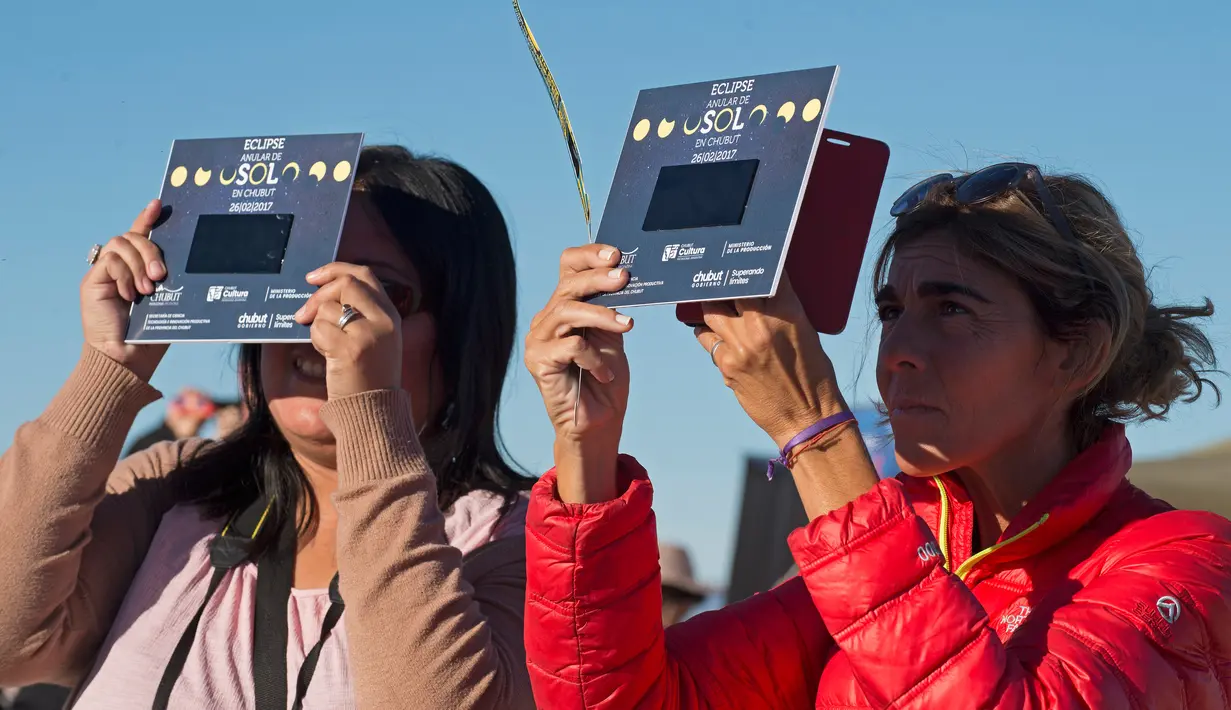 Dua orang wanita melihat gerhana matahari annular dengan alat khusus di Estancia El Muster, Argentina (26/2). Menggunakan teleskop khusus, kaca mata pelindung, atau perangkat buatan sendiri, mereka menyaksikan fenomena alam tersebut. (AFP/Alejandro Pagni)