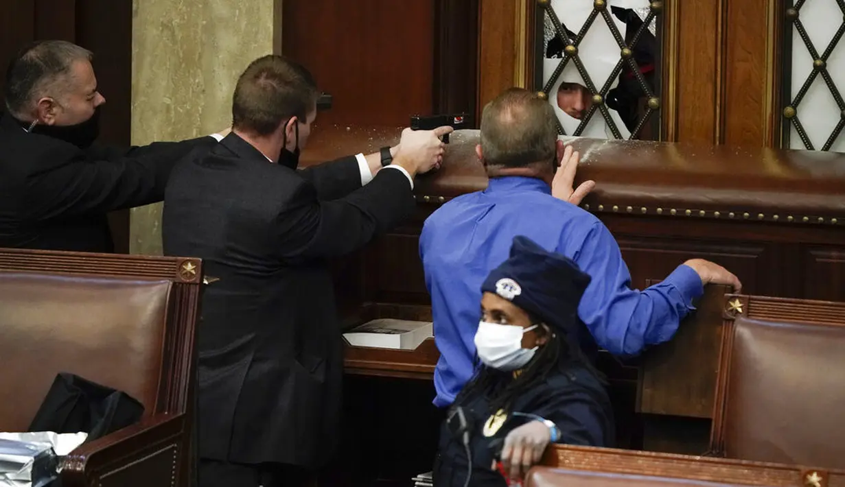 Polisi berdiri dekat pintu sambil menodongkan pistol saat pengunjuk rasa mencoba masuk ke Gedung Capitol Hill di Washington DC, Amerika Serikat, Rabu (6/1/2021). Pengunjuk rasa berusaha mengganggu proses penghitungan Kongres atas suara Electoral College. (AP Photo/J. Scott Applewhite)