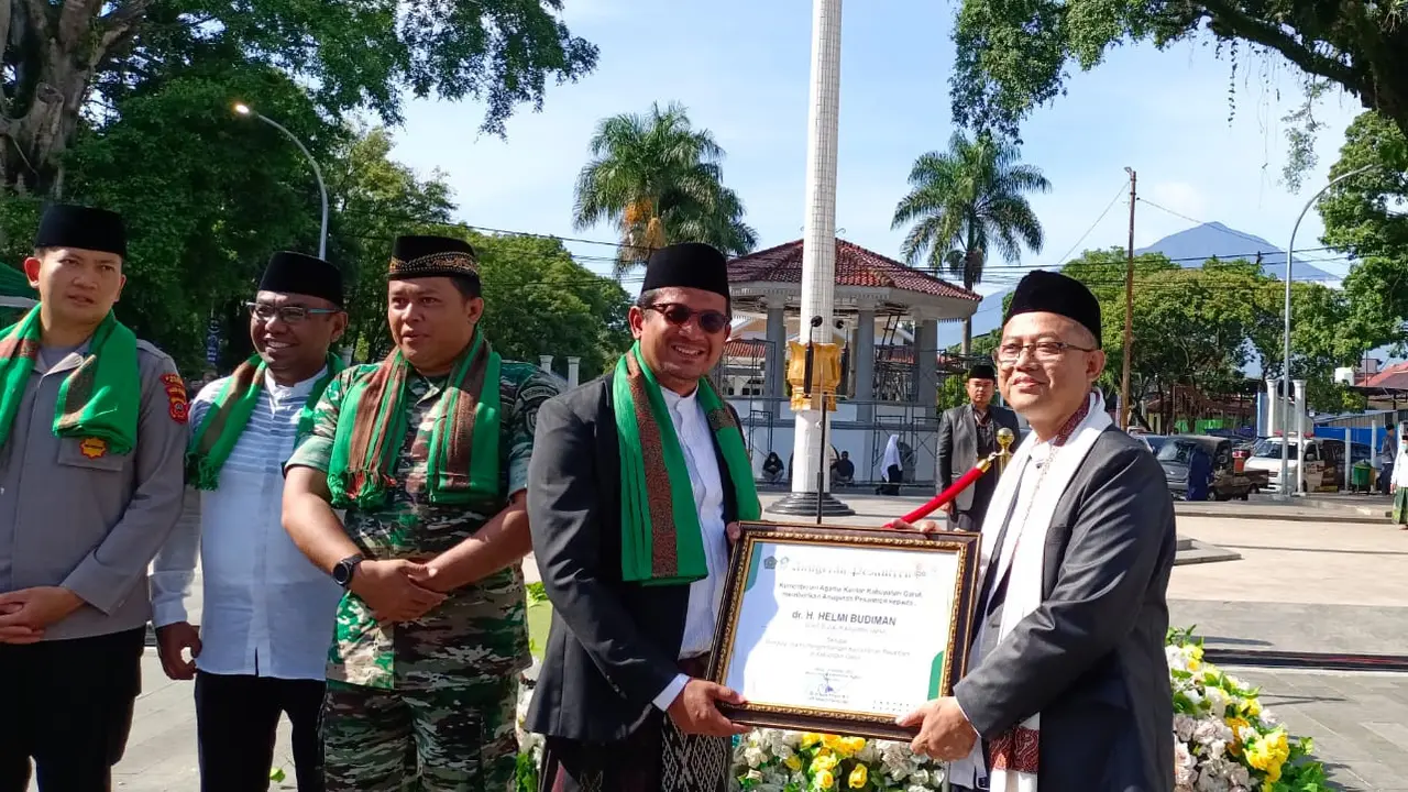 Kamenag Garut Cece Hidayat menyerahkan penghargaan kepada Wabup Garut Helmi Budiman dalam puncak perayaan upacara Hari Santri Nasional (HSN) 2022 di Garut. (Liputan6.com/Jayadi Supriadin)
