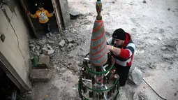 Akram Abu al-Foz menghias sebuah pohon Natal buatannya di wilayah yang dikuasai oposisi di Douma, Suriah, Jumat (23/12). Pohon Natal itu terbuat dari sisa-sisa amunisi perang antara pemberontak dan pasukan rezim Bashar Al Assad. .(REUTERS/Bassam Khabieh)