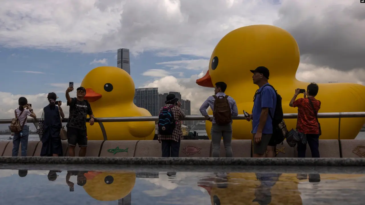 Anggota masyarakat memotret instalasi seni "Double Duck" seniman Belanda Florentijn Hofman di Pelabuhan Victoria, Hong Kong, Jumat, 9 Juni 2023. (AP/Louise Delmotte)