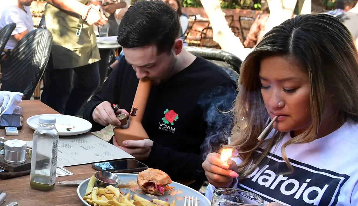 Will Halverson (kiri) merokok dari sebuah bong ketika Mimi Bui menyalakan ganja sehari sebelum pembukaan resminya di Lowell Cafe di Hollywood Barat, California  (30/9/2019).  Pengunjung dapat merokok ganja di kafe dengan menggunakan sendi, pipa, dan bong. (AFP Photo/Frederic J. Brown)