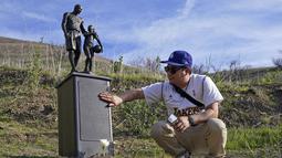 Oscar Romero menyentuh patung untuk mengenang Kobe Bryant dan putrinya, Gianna di Calabasas, California, Rabu (26/1/2022). Patung tersebut dibawa seniman Dan Medina, di jalan setapak dekat lokasi Bryant, putrinya dan tujuh orang lainnya tewas dalam kecelakaan helikopter pada 2020. (AP/Ashley Landis)