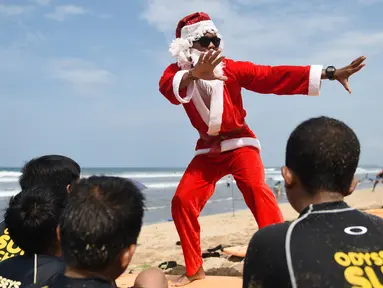 Seorang pria berkostum Santa Claus memberikan pelatihan selancar kepada sejumlah anak di Pantai Kuta, Bali, Senin (10/12). Setiap tahunnya, ribuan wisatawan mendatangi Bali saat menjelang natal dan tahun baru. (AFP PHOTO / Sonny Tumbelaka)