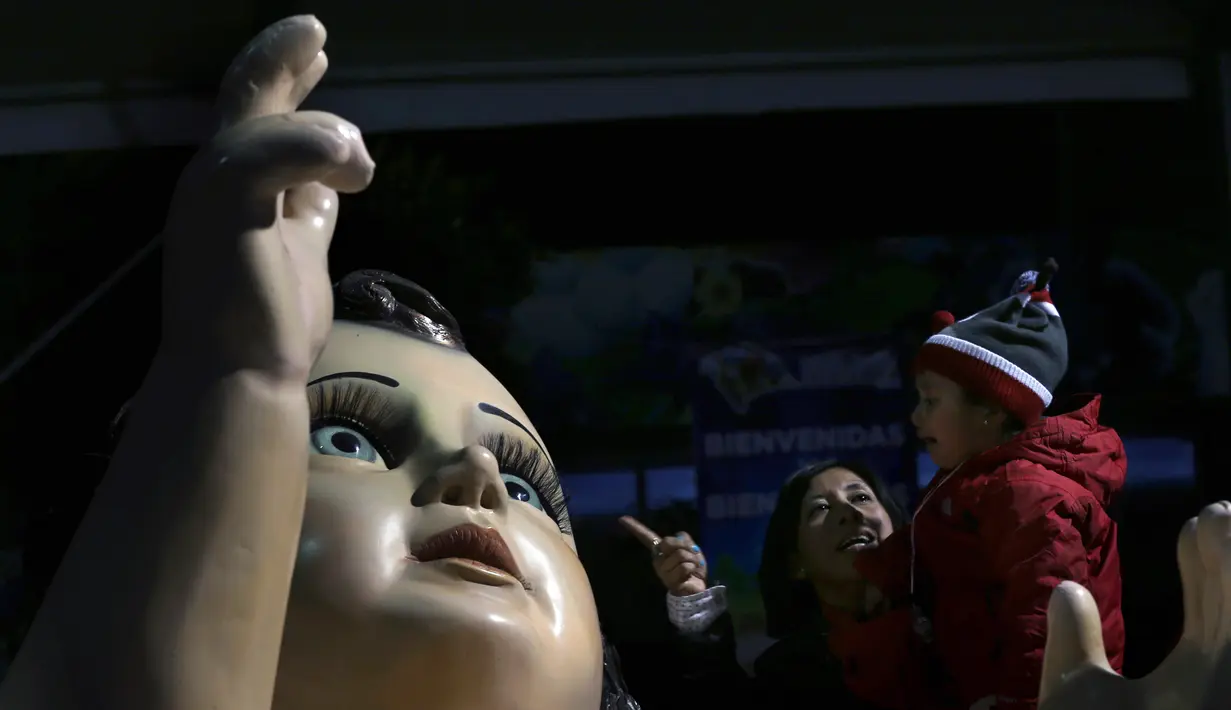 Seorang ibu berbicara dengan putranya dekat patung bayi Yesus raksasa di Mexico City, Meksiko, Senin (23/12/2019). Patung tersebut dipersiapkan untuk menyambut malam Natal. (AP Photo/Marco Ugarte)