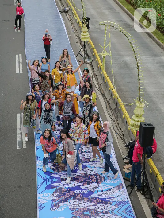Sejumlah orang yang mengenakan batik berpose di catwalk Jalan Jenderal Sudirman, Jakarta, Minggu (2/10/2022). Kegiatan yang diikuti ratusan orang ini diselenggarakan oleh Bank Mandiri untuk menyambut Hari Batik Nasional yang jatuh setiap tanggal 2 Oktober 2022. (Liputan6.com/Faizal Fanani)