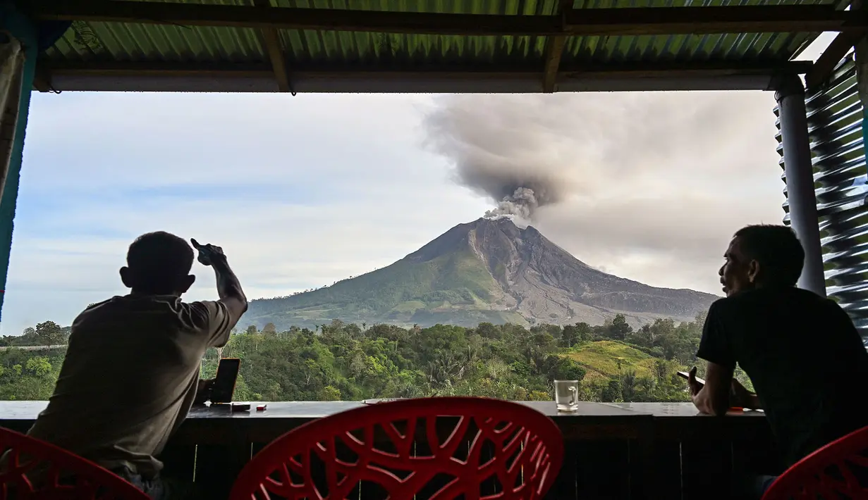 Dua pria menyaksikan Gunung Sinabung menyemburkan abu dan asap tebal dari wilayah Karo, Provinsi Sumatra Utara, Rabu, 2 September 2026. (AFP/ YT Haryono)