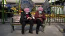 Wanita memakai masker untuk melindungi diri dari COVID-19 melihat smartphone mereka di taman umum di Beijing, Rabu (5/1/2022). China melaporkan penurunan besar infeksi COVID-19 lokal di kota utara Xi'an, yang telah dikunci ketat selama dua minggu terakhir. (AP Photo/Mark Schiefelbein)
