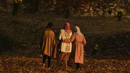Para wanita berjalan melewati pepohonan yang merontokkan daun musim gugur mereka di taman Nishat Bagh di Srinagar (16/11/2020). (AFP/Tauseef Mustafa)