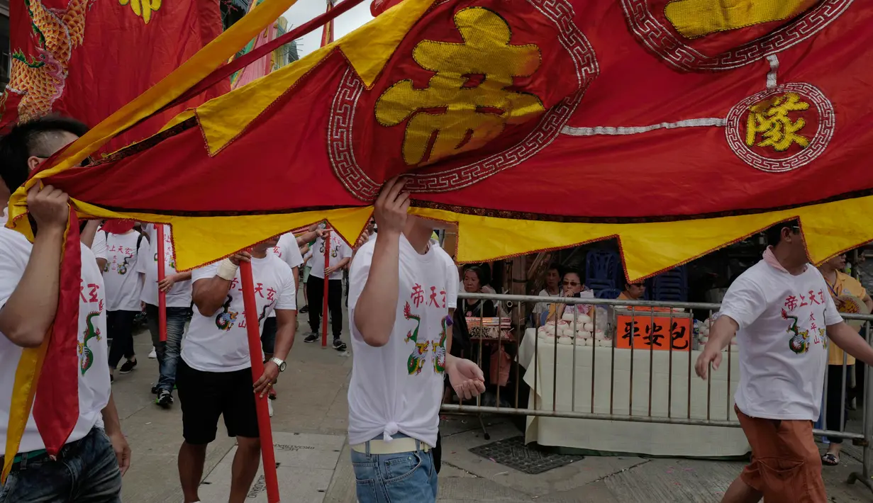 Penduduk setempat membawa bendera saat merayakan Festival Cheung Chau Bun di Hong Kong (5/3). Dulunya, festival ini digelar sebagai bentuk permohonan perlindungan dewa karena seringnya penyerangan yang dilakukan oleh para bajak laut. (AP Photo/Vincent Yu)