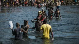 Para migran menyeberangi Rio Grande dari Del Rio, Texas, ke Ciudad Acuña, Meksiko, untuk berbelanja makanan sebelum kembali ke sisi perbatasan AS, Minggu (19/9/2021). Ribuan migran Haiti telah tiba di Del Rio, Texas, saat pihak berwenang berupaya menutup perbatasan.(AP Photo/Felix Marquez)