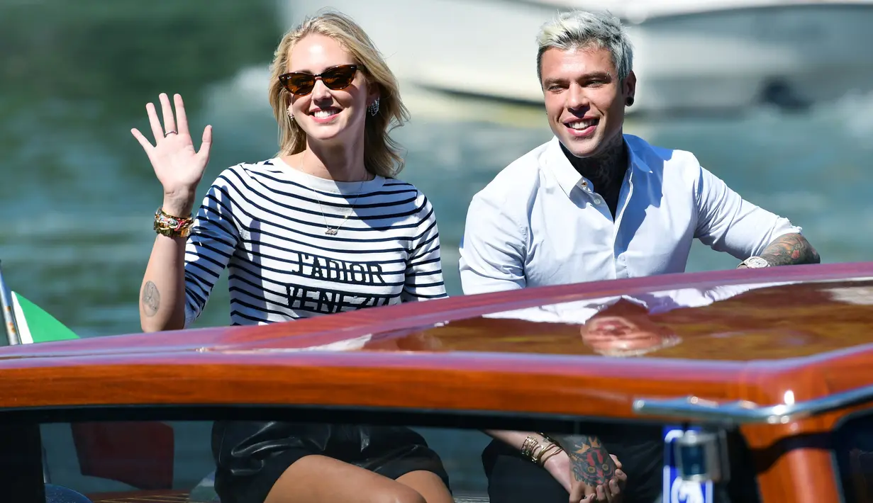 Blogger sekaligus perancang busana Chiara Ferragni (kiri) bersama suaminya rapper Federico Leonardo Lucia atau Fedez melambaikan tangan saat tiba untuk menghadiri Venice Film Festival 2019 di Dermaga Hotel Excelsior, Venesia, Italia, Selasa (3/9/2019). (Alberto PIZZOLI/AFP)