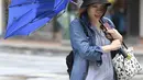 Seorang wanita membawa payungnya yang rusak saat berjalan melawan angin kencang yang ditimbulkan oleh topan Lekima di Taipei, Taiwan (9/8/2019). Topan  tersebut dinilai sebagai yang terkuat menghantam Taiwan di tahun ini. (AFP Photo/Sam Yeh)